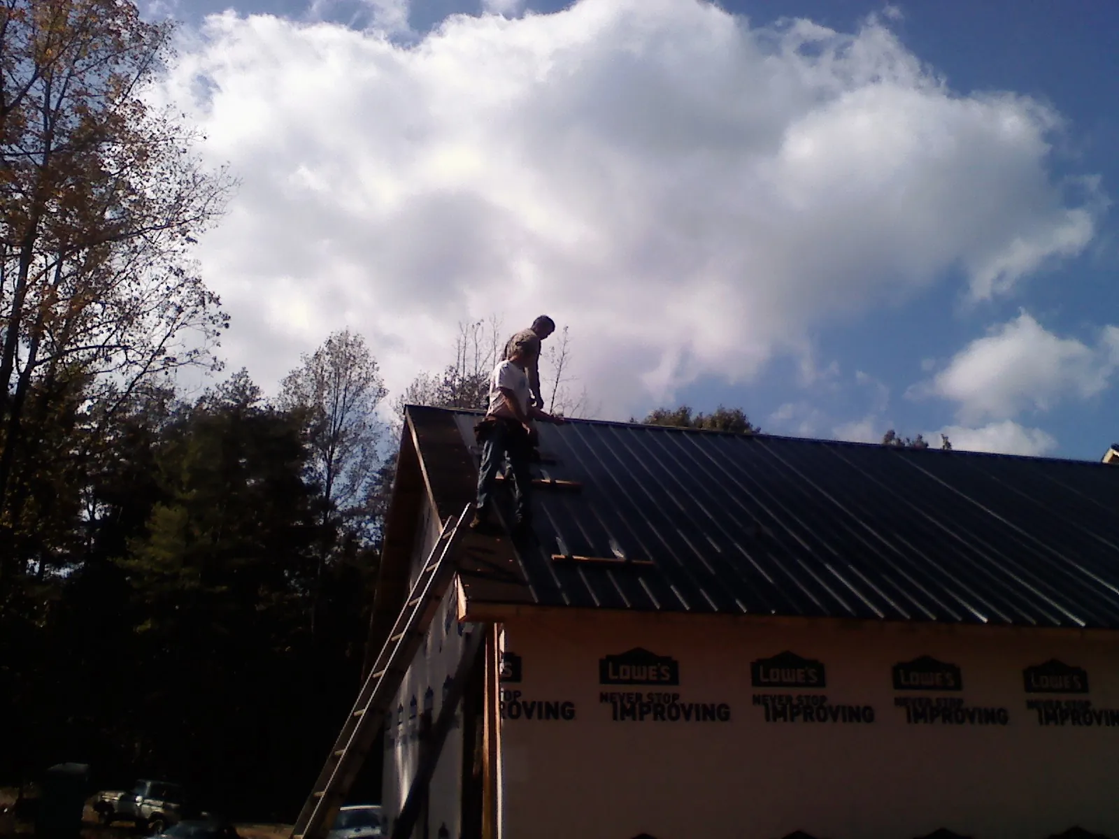 Roofer fastening dark metal panels high against a cloudy sky, from a Roof Inspection job in Reddick