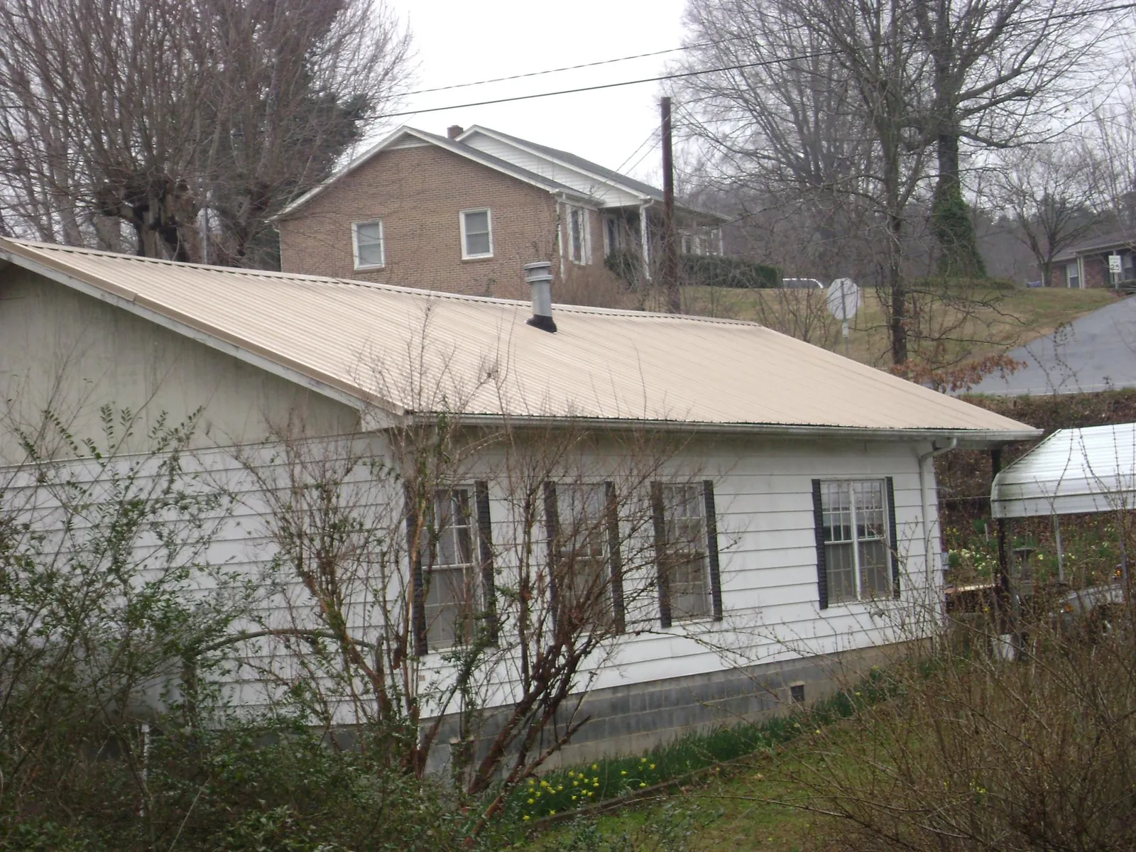 Tan metal roof on a white sided house set into a hillside — Commercial Roofing by Roofing Brothers in Reddick